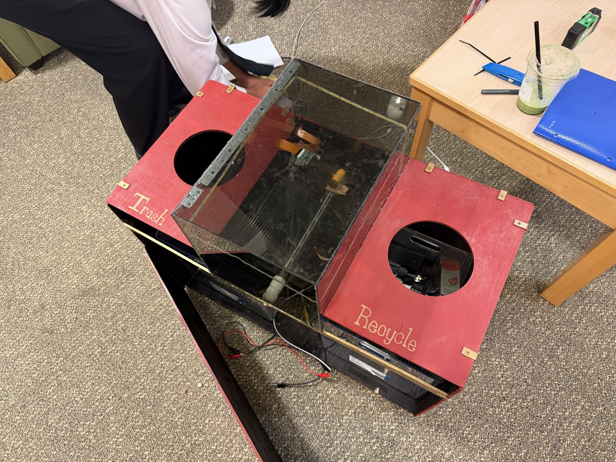 The finished sorter from above: a clear polycarbonate intake chamber between two red lids labeled Trash and Recycle, on a black-painted wood base.