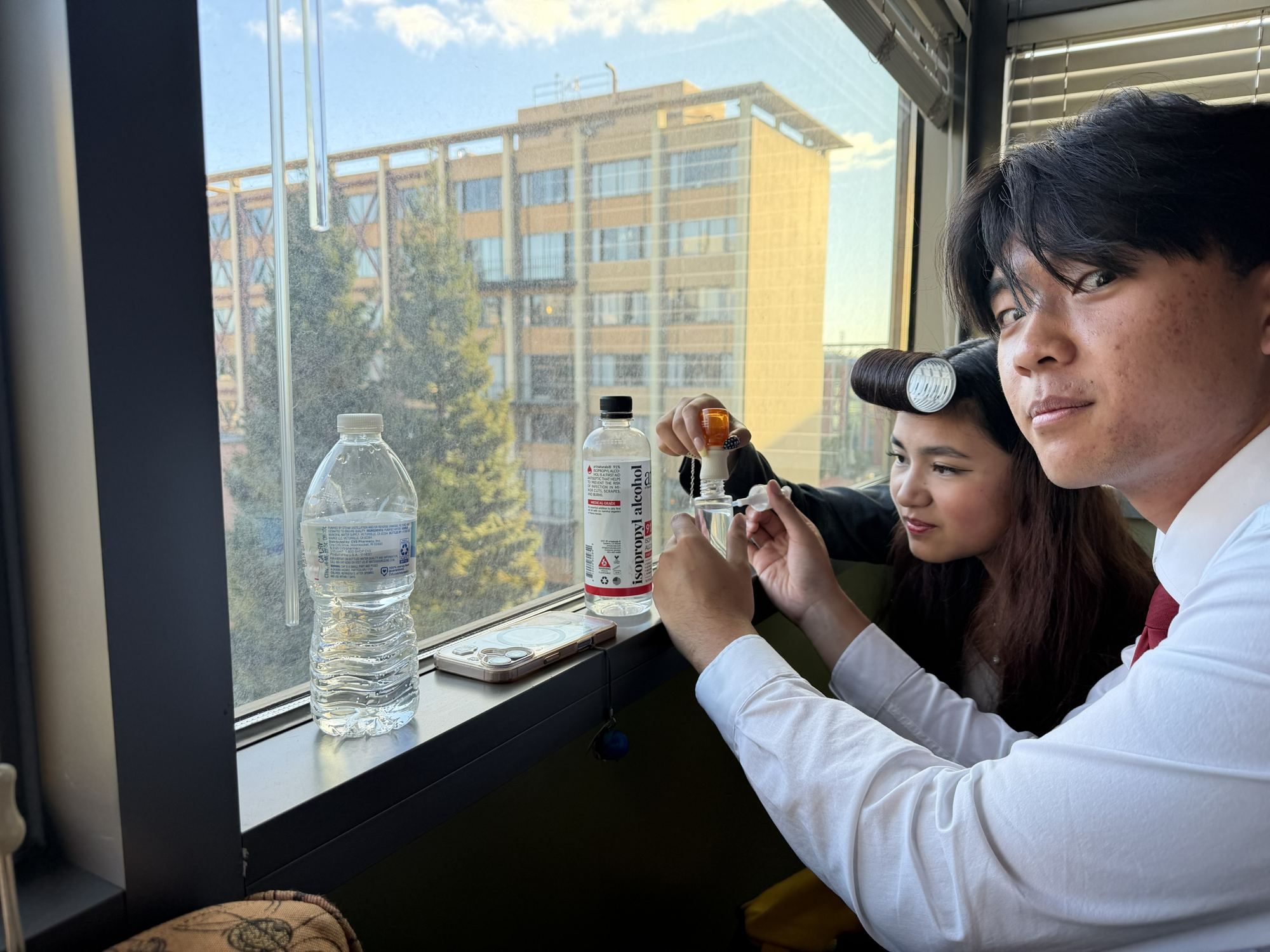 Two team members measuring isopropyl alcohol into a spray bottle by a window.