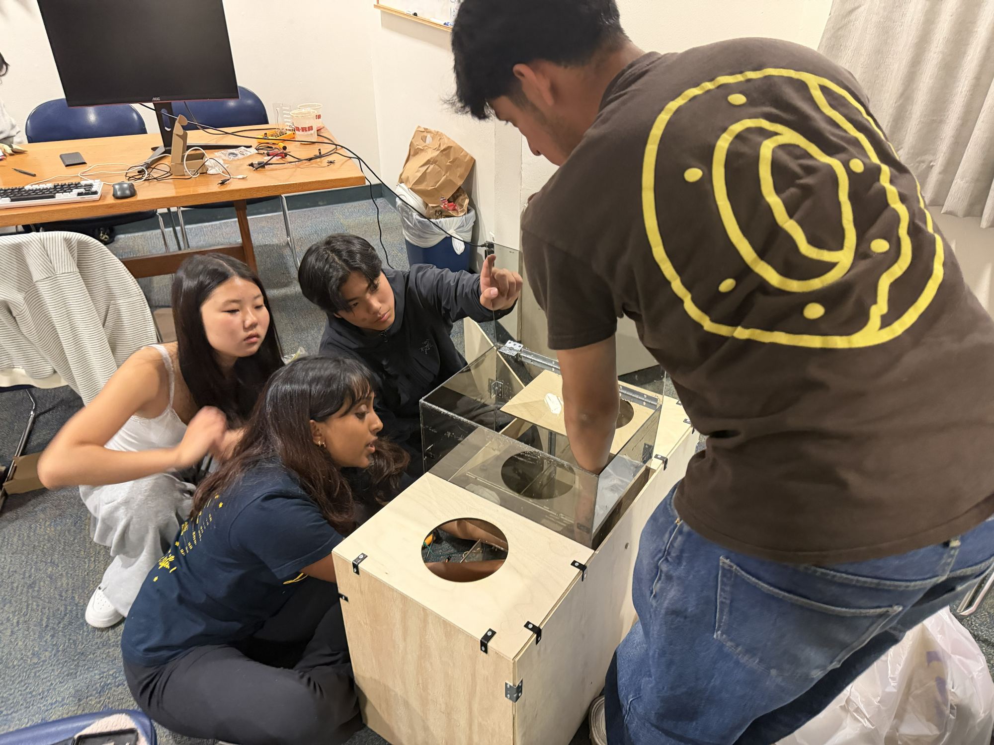 Four team members assembling the unpainted plywood enclosure with the clear intake box on top.