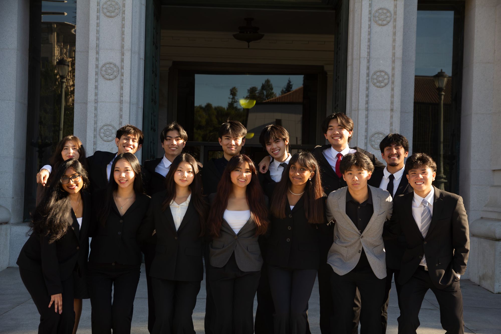 The fourteen team members in business attire in front of a campus building.